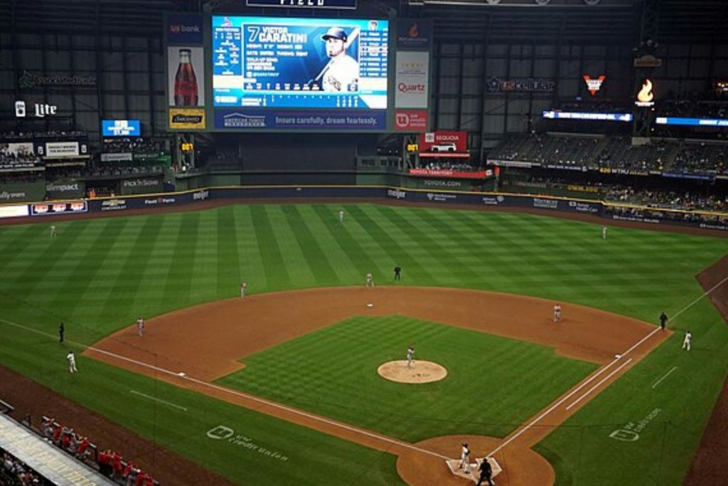 경기장에서 진행 중인 야구 경기로, 커다란 전자 점수판에 선수 정보가 표시됩니다.