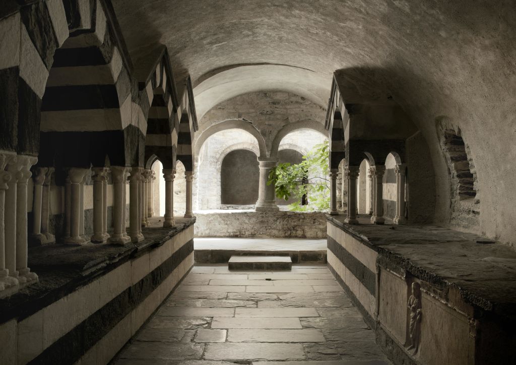 줄무늬와 아치형 기둥이 있는 돌 복도는 푸른 나무가 있는 안뜰로 이어집니다. 단계는 아치형 개구부에서 내려옵니다.