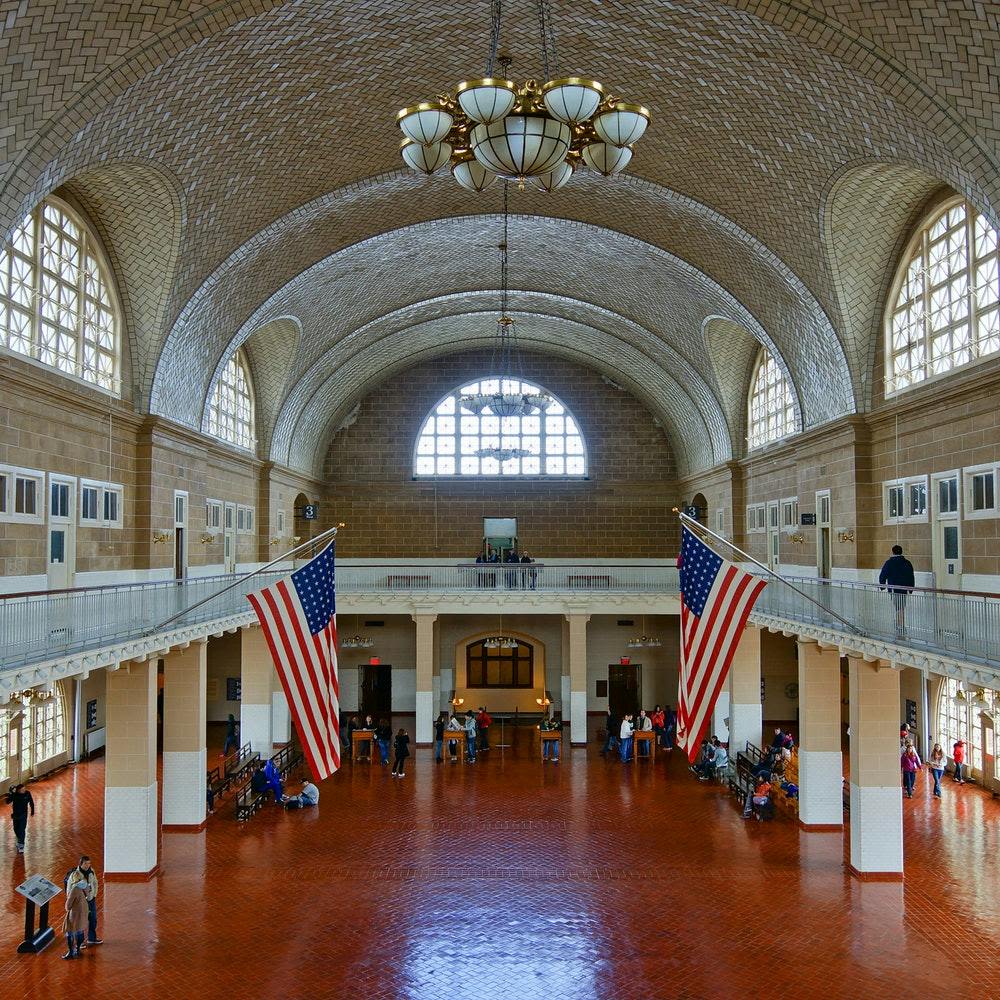 아치형 천장, 샹들리에, 미국 국기가 있는 크고 유서 깊은 홀. 사람들이 숙소 주변에 흩어져 있습니다.