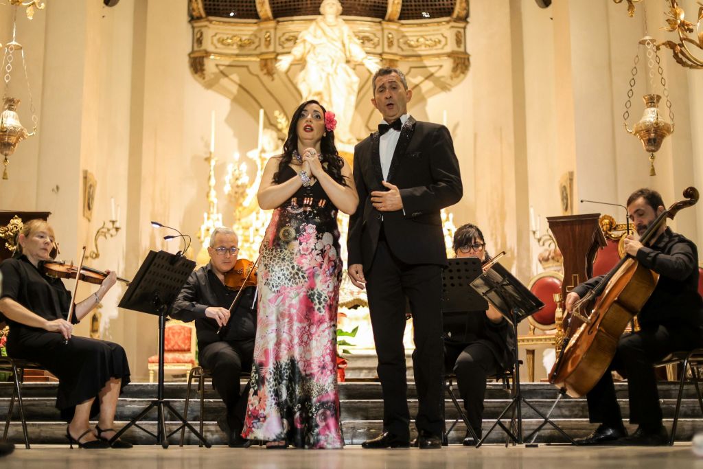 두 명의 가수가 무대에서 정장 차림으로 공연하고, 세 명의 뮤지션이 현악기를 연주하며 화려한 분위기를 연출합니다.