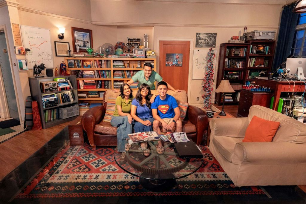 책장과 과학 모델, 다양한 인테리어 소품이 가득한 거실에 4명이 소파에 앉아 있습니다. 앞에 커피 테이블이 있습니다.