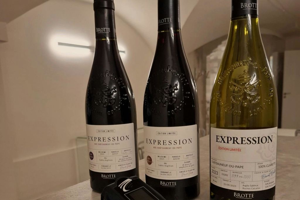 디지털 기기 옆 테이블에 노란색 1개와 어두운색 2개가 놓인 '익스프레션 (Expression)' 라벨이 붙은 브로트 와인 3병.