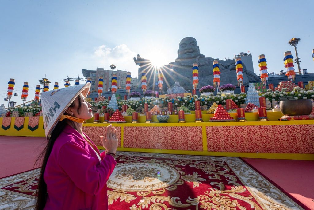 전통 의상을 입은 사람이 화려한 장식과 커다란 앉아 있는 모습의 동상이 있는 제단 앞에서 기도하고 있습니다.