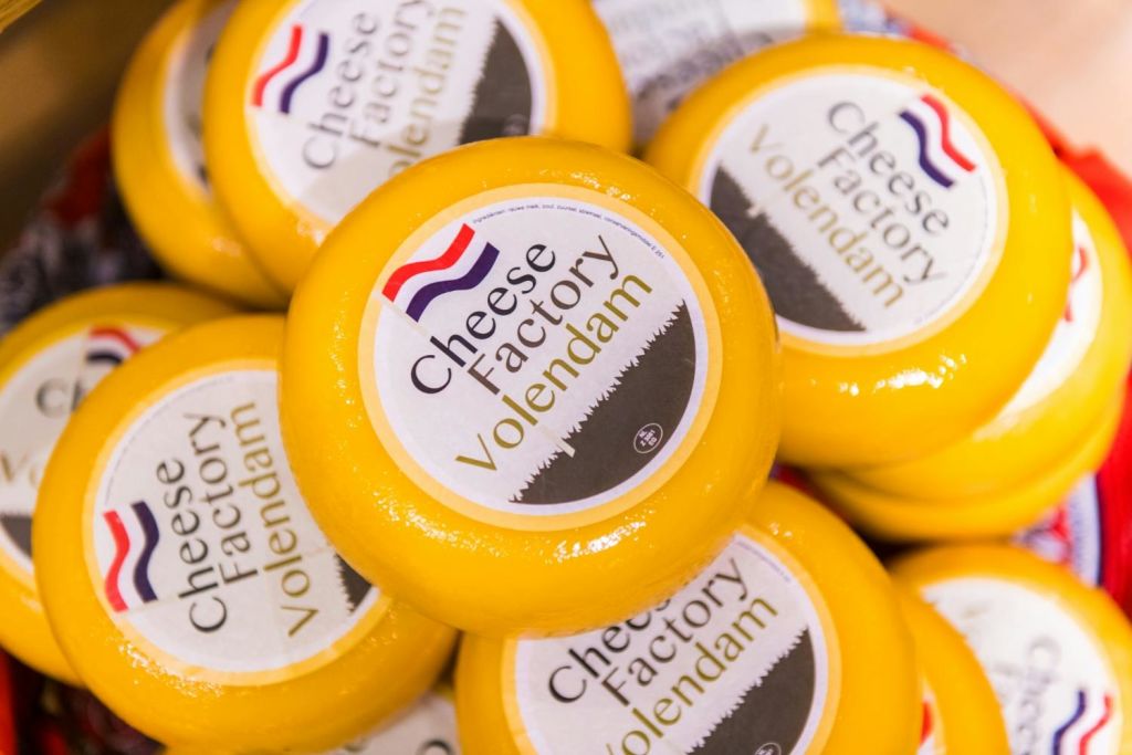 네덜란드 국기가 새겨진 로고가 있는 "Cheese Factory Volendam" 라벨이 붙은 노란색 치즈 라운드가 쌓여 있습니다.