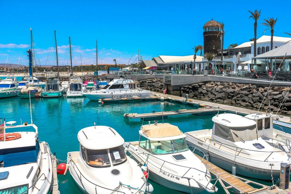 맑고 푸른 하늘 아래 배경으로 석조 건물, 상점, 카페가 있는 정박지에 배가 정박해 있습니다.