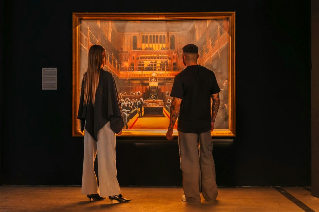 한 부부가 전시회에서 뱅크시의 그림 중 하나를 감상합니다.