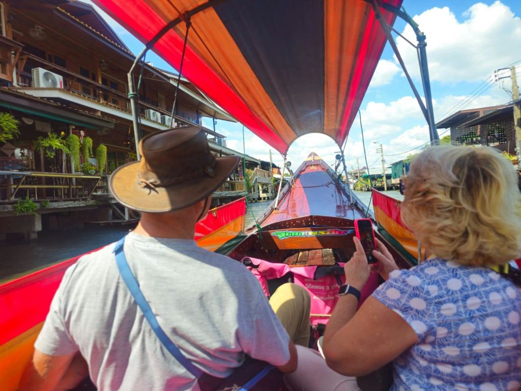 한 사람이 사진을 찍고 있는 가운데, 두 사람이 운하의 화려한 보트에 앉아 있습니다. 건물은 운하의 양쪽에 줄지어 있습니다.