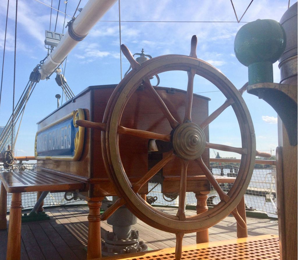 부분적으로 흐린 하늘 아래에서 밧줄과 리깅이 있는 돛단배의 갑판에 있는 나무 배의 바퀴.