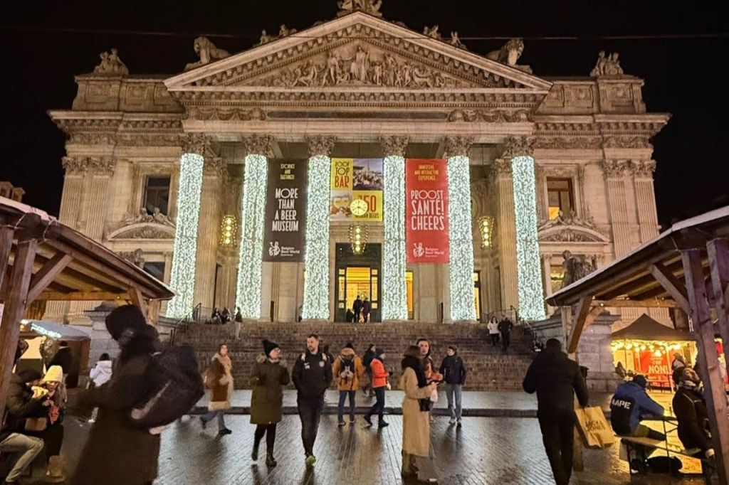 조명이 밝은 신고전주의 양식의 건물 앞을 걷는 사람들로, 밤에는 현수막과 조명 기둥이 있습니다.
