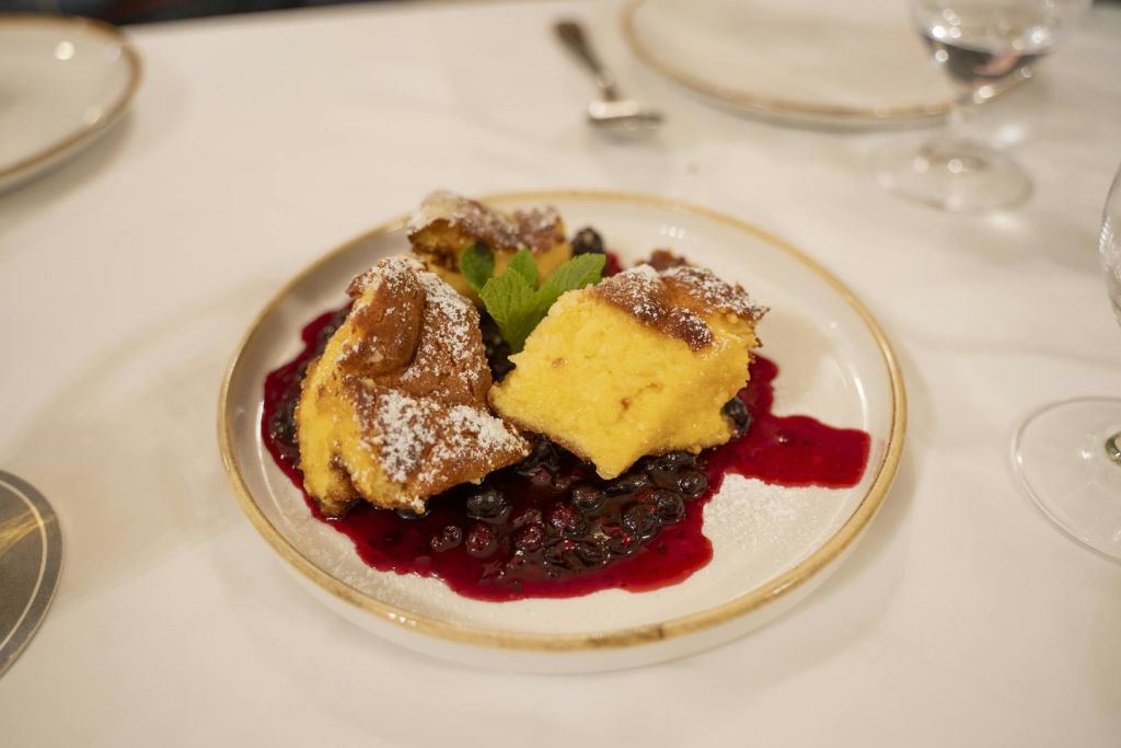 민트 잎으로 장식된 베리 컴포트 침대에 설탕 가루로 가루 낸 페이스트리 조각이 담긴 접시.