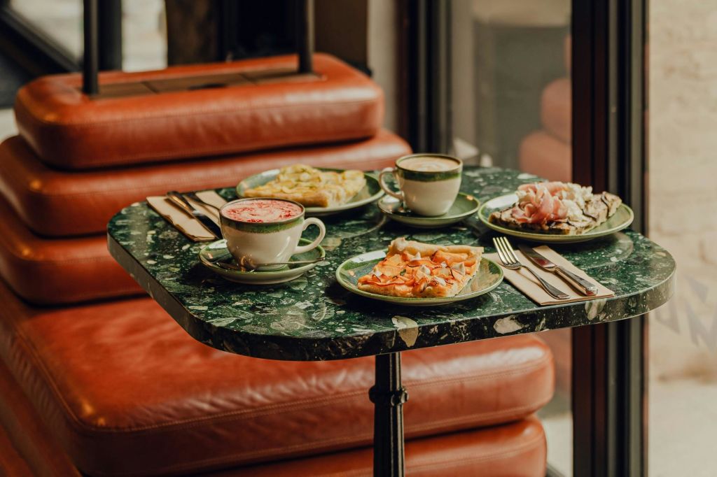 베를린 포토그라피스카 (Fotografiska Berlin) 의 카페 바에서 촬영한 가죽 소파 앞에 접시 3개와 커피 두 잔이 놓인 테이블 이미지