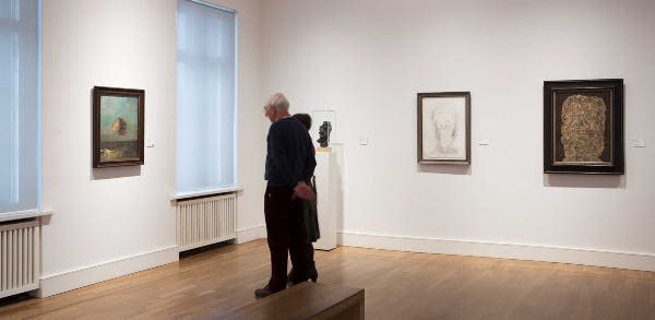 두 사람이 미술관에 서서 벽에 액자 그림과 받침대 위에 조각된 머리를 보고 있습니다.