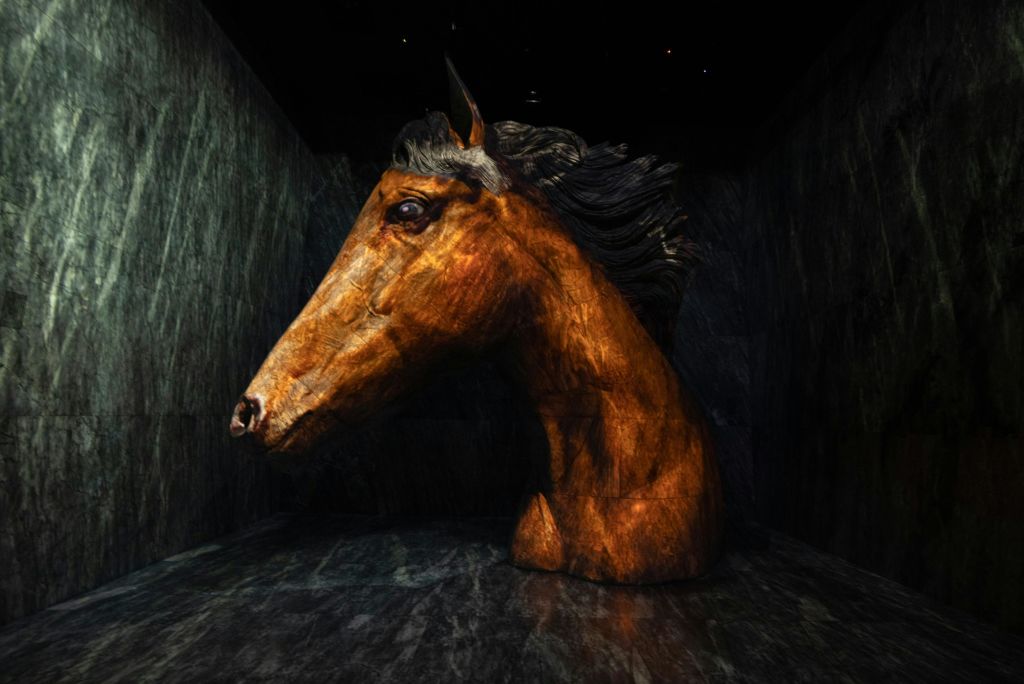어두운 벽과 바닥이 있는 조명이 희미한 방에 전시된 크고 세밀한 말의 머리 조각.