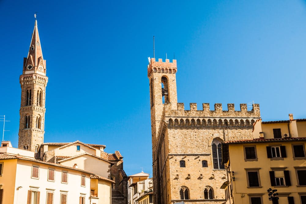 맑고 푸른 하늘을 배경으로 우뚝 솟은 탑이 있는 유서 깊은 석조 건물, 타일로 덮인 지붕이 있는 주변 건물.