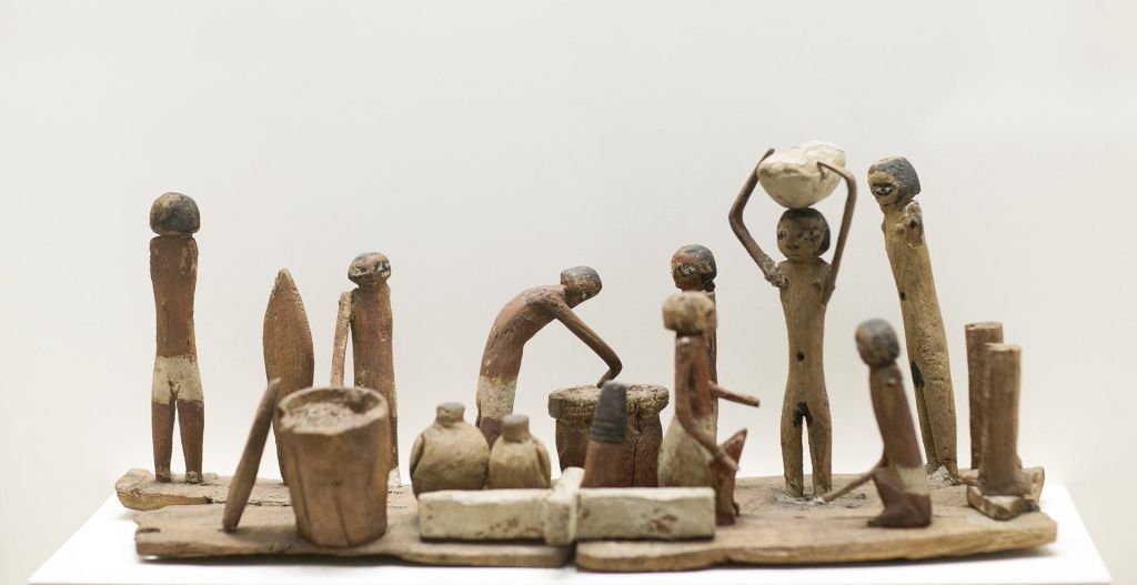 작은 나무 조각상은 평범한 배경으로 바구니와 화분을 들고 다니는 등 다양한 활동에 참여하는 사람들을 묘사합니다.