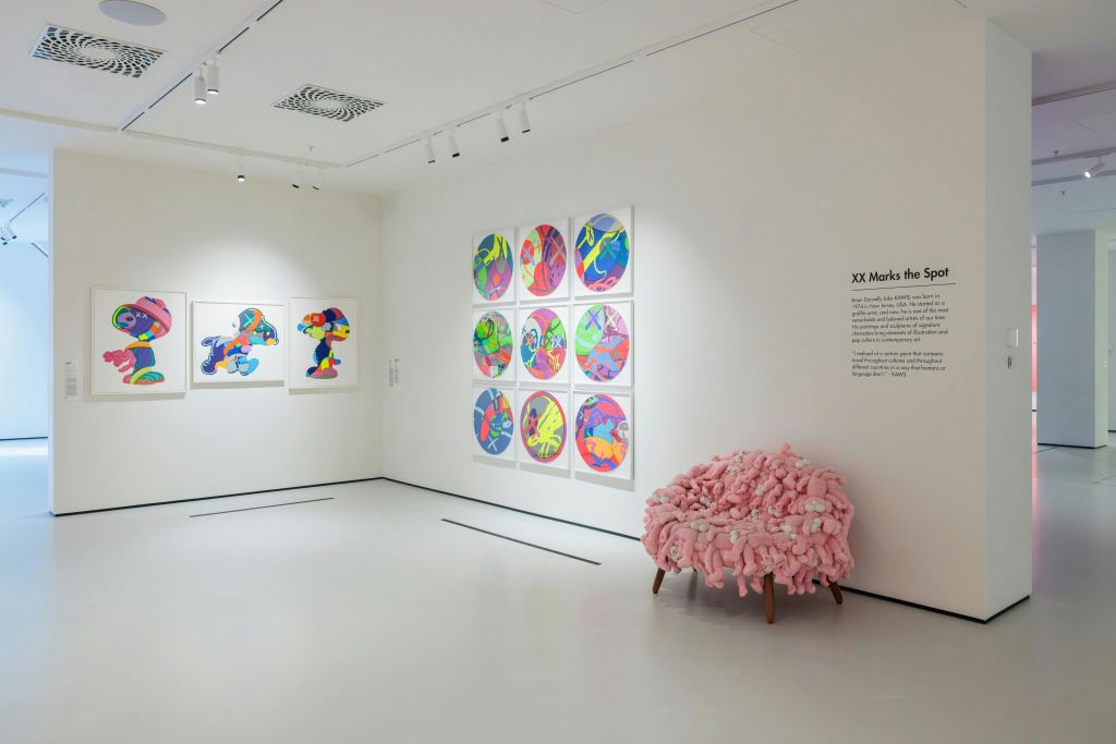 벽에는 다채로운 추상 미술 작품이 전시되어 있고, 모퉁이에는 분홍색 질감의 의자가 있습니다.