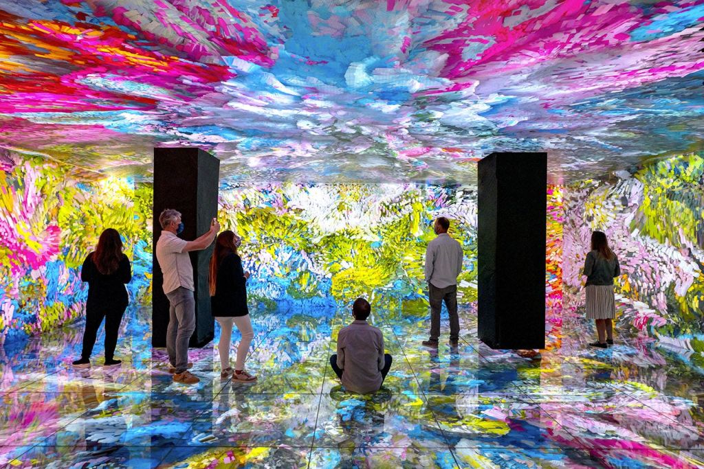 사람들은 벽, 바닥, 천장에 화려하고 추상적인 패턴이 있는 생동감 있고 몰입감 있는 예술 작품에 감탄합니다.