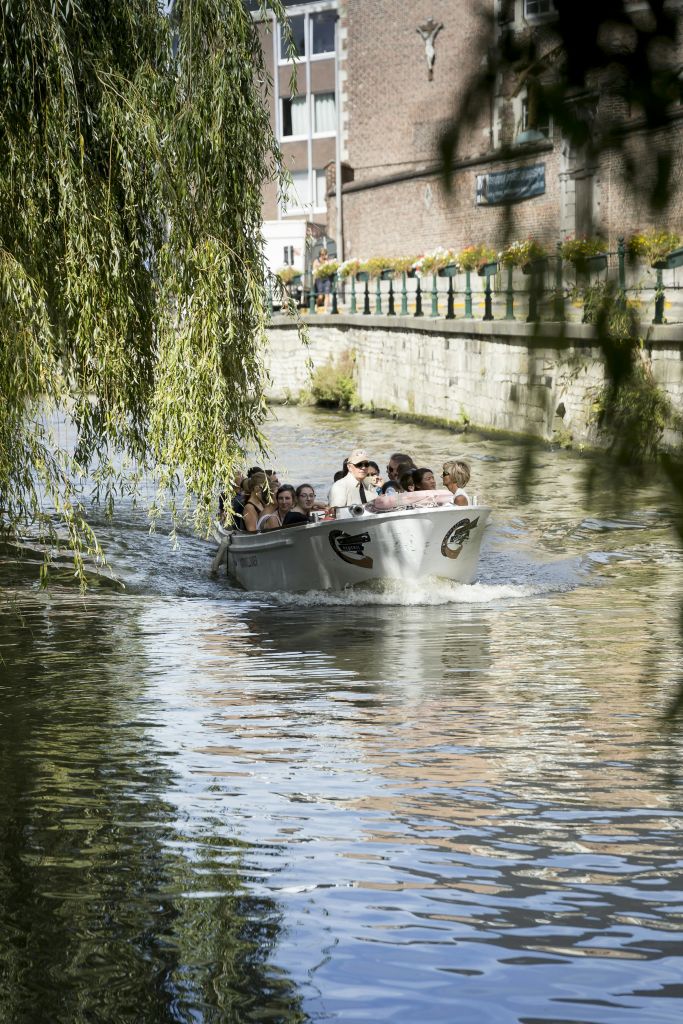 한 무리의 사람들이 잔잔한 운하에서 보트를 타고 울부짖는 버드나무 가지가 매달려 있고 근처에 벽돌로 된 해안이 있습니다.
