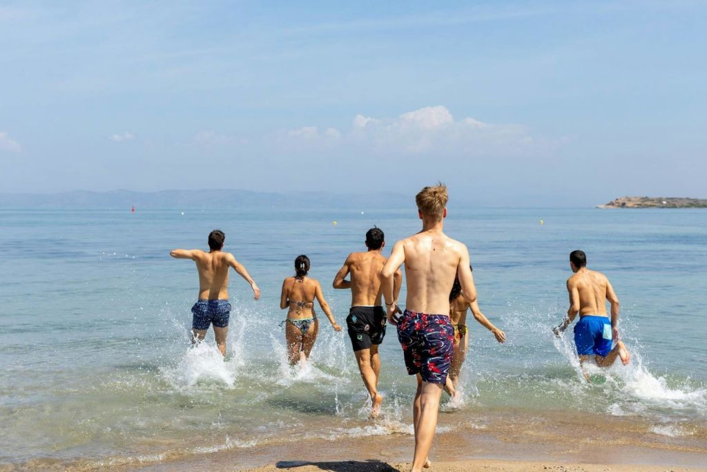한 무리의 젊은이들이 함께 화창한 해변의 하루를 즐기며 바다로 뛰어들어 물을 튀깁니다.