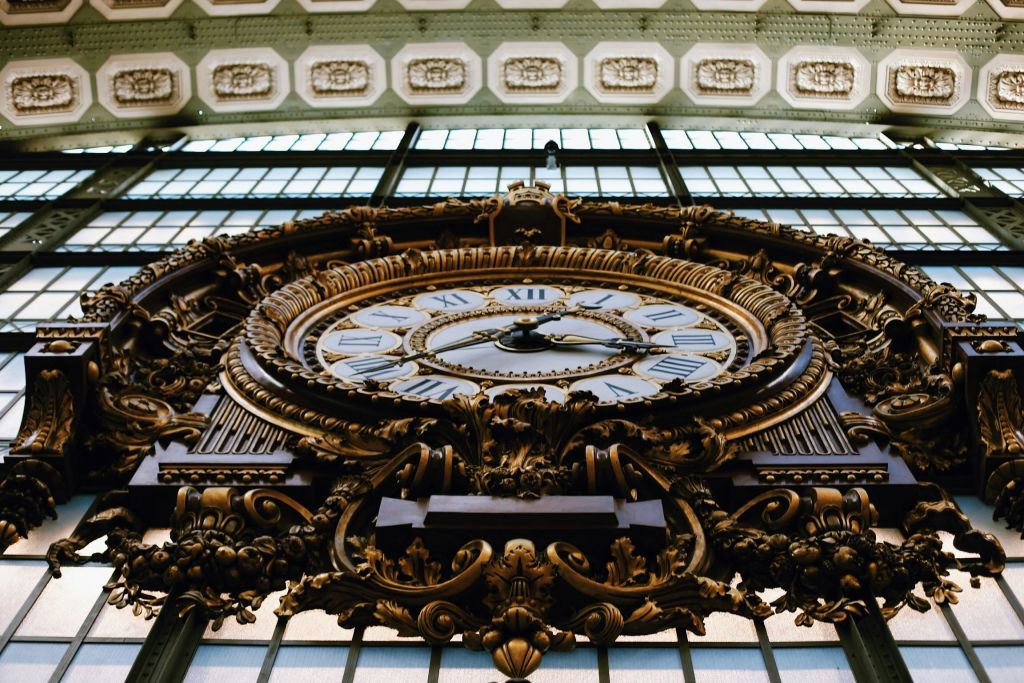 커다란 유리 패널 벽에 장식용 골드 프레임으로 장식된 로마 숫자가 장식된 화려한 앤티크 시계.