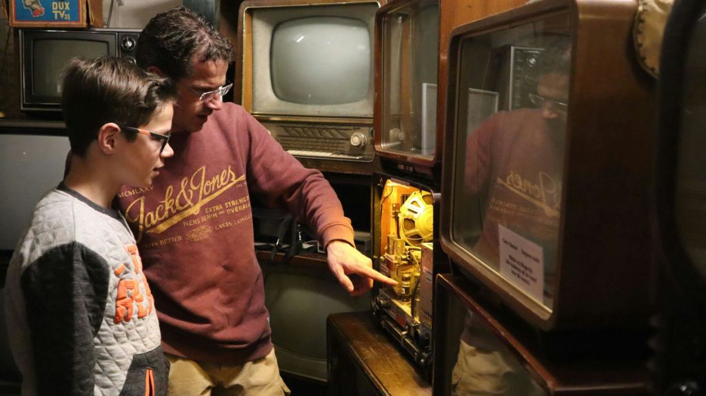 오래된 텔레비전으로 가득 찬 방에서 한 남자와 한 소년이 빈티지 기기를 살펴보고 있습니다.