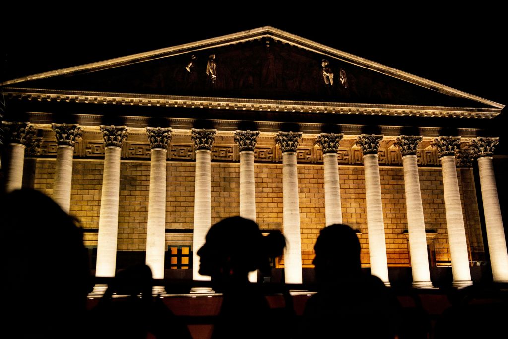 밤에 높은 기둥이 있는 조명이 있는 신고전주의 건물 앞에 있는 사람들의 실루엣.