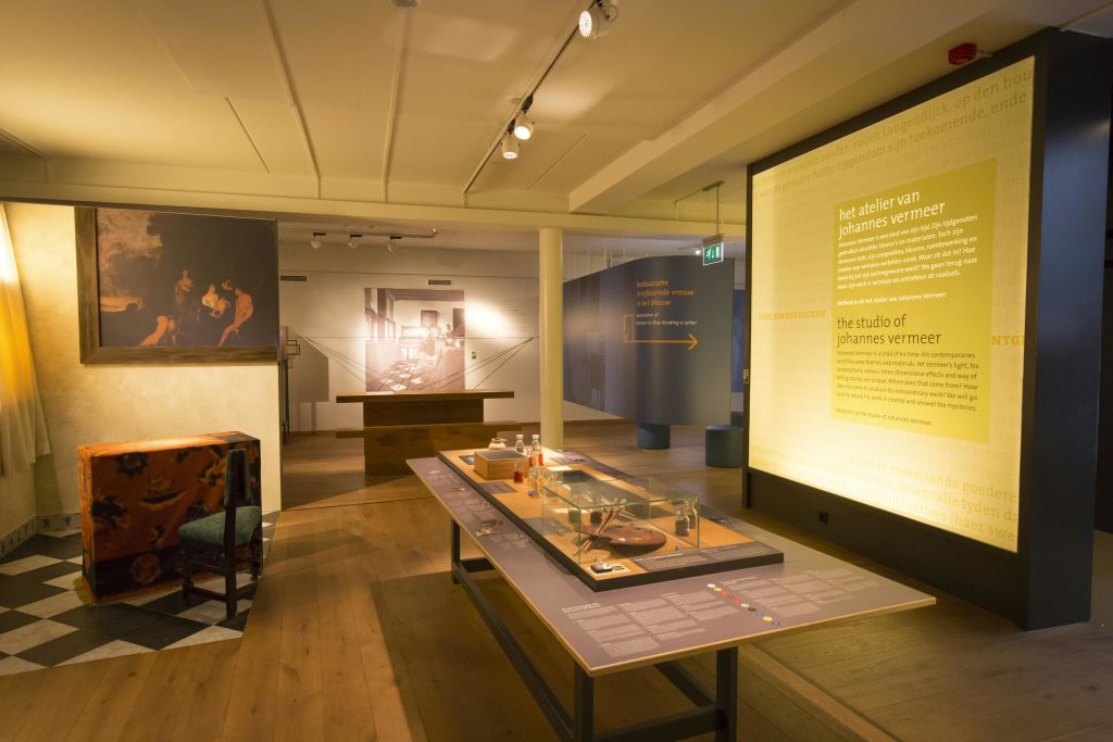 텍스트 패널, 사진, 중앙 테이블 등 요하네스 베르메르에 대한 정보가 전시된 박물관 전시실입니다.