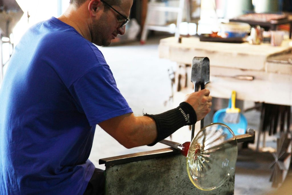 공방에서 금속 공구로 녹은 유리를 형상화한 파란색 셔츠를 입은 사람.