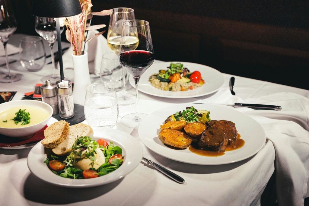 음식 접시, 레드 와인 및 화이트 와인 한 잔, 물 한 잔이 담긴 흰색 식탁보가 있는 우아한 식탁.