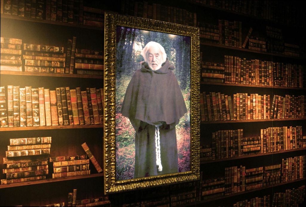 흰 수염과 가운을 두른 승려의 액자 초상화가 낡은 책장이 늘어선 벽에 걸려 있습니다.