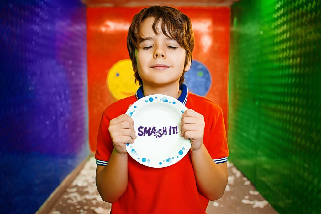 빨간 셔츠를 입은 한 소년이 바닥에 조각난 화려한 방에서 "부숴버려!" 라고 쓰인 접시를 들고 있습니다.