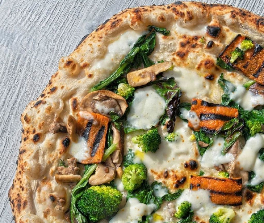 나무 표면에 브로콜리, 시금치, 버섯, 녹인 치즈 등 구운 야채를 얹은 피자.