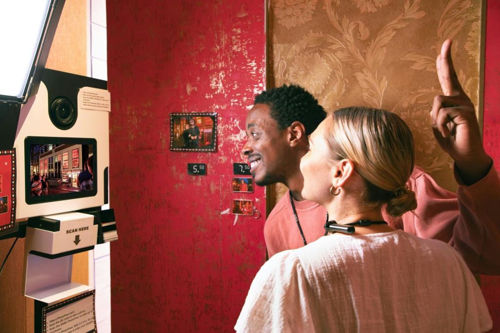 두 사람이 질감이 살아있는 벽지로 장식된 벽에 걸린 사진을 바라보고 있습니다. 벽을 배경으로 손짓이 위를 향하고 있습니다.