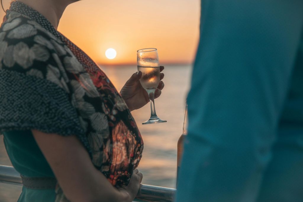 바다 너머로 지는 석양을 배경으로 와인 한 잔을 들고 다른 사람 옆에 서 있는 사람.