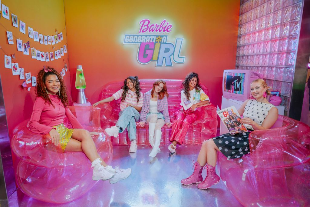 "Barbie Generation Girl" 간판과 MTV 테마 TV가 있는 밝은 방에서 분홍색 팽창식 가구에 앉아 있는 네 명의 여성.