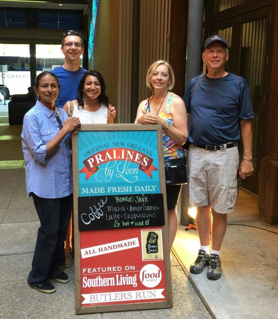 도시 보도의 "Pralines by Leon" 표지판을 둘러보며 웃고 있는 5명의 일행.