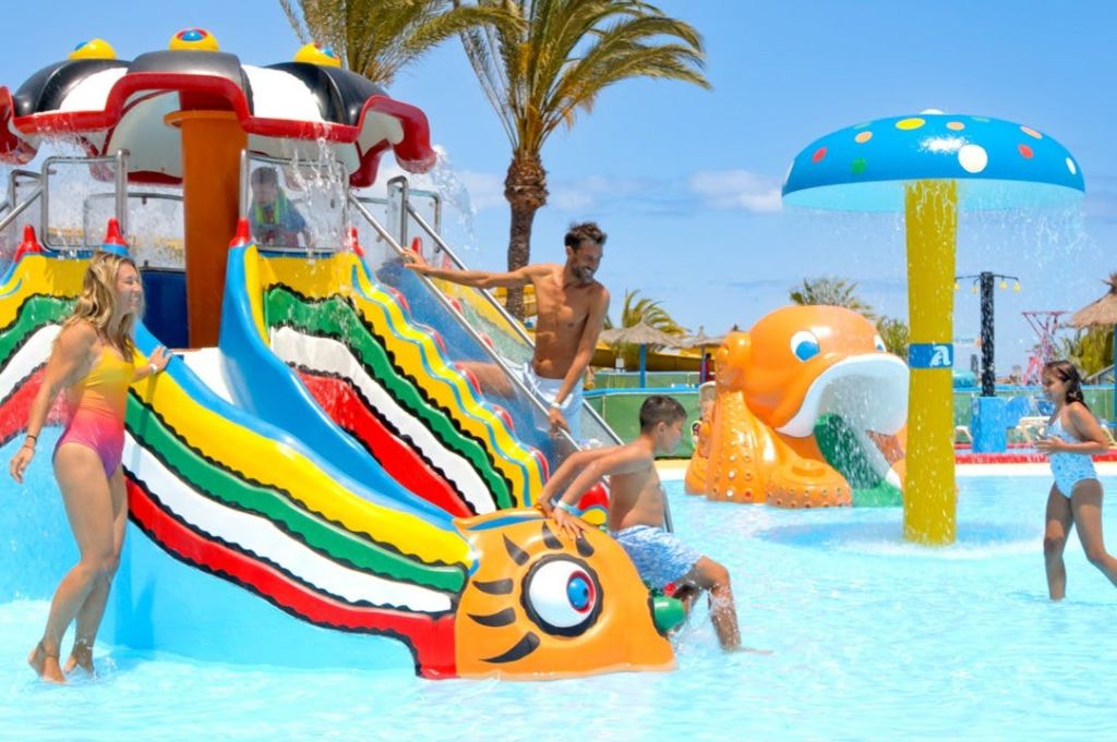 햇살이 내리쬐는 야외 워터파크에서 애벌레 모양의 다채로운 워터 슬라이드에서 놀고 있는 어린이와 성인.