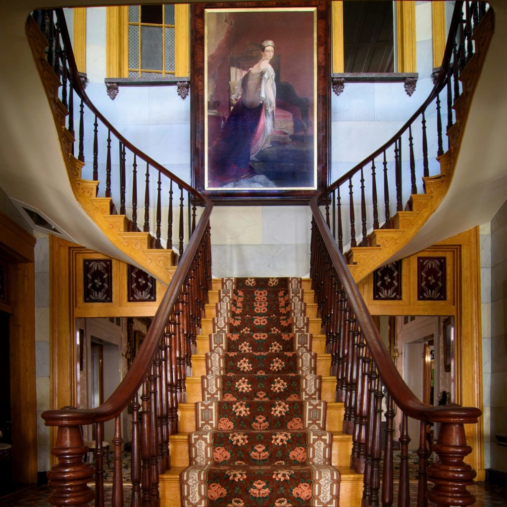 나무 난간이 구부러진 우아한 계단, 화려한 카펫, 착륙장에서 찍은 커다란 여성 초상화.