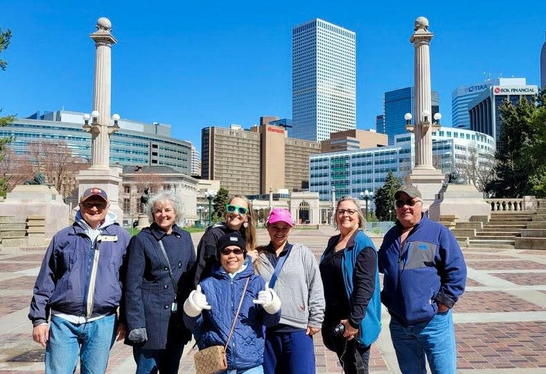 높은 건물과 기둥이 달린 기념비를 배경으로 한 도시 광장에는 6명의 사람들이 야외에 서 있습니다.