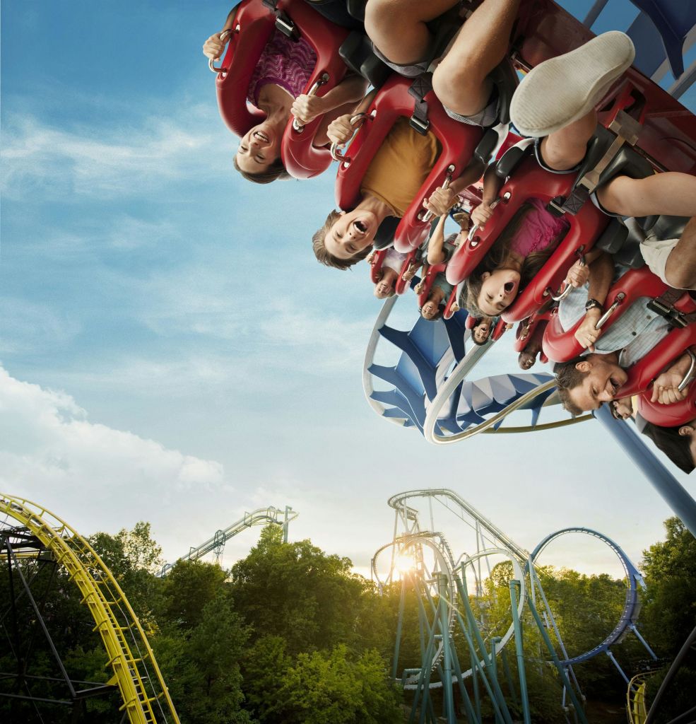 롤러코스터를 거꾸로 타고 비명을 지르며 웃는 사람들. 푸른 하늘과 다른 롤러코스터 트랙을 배경으로 합니다.