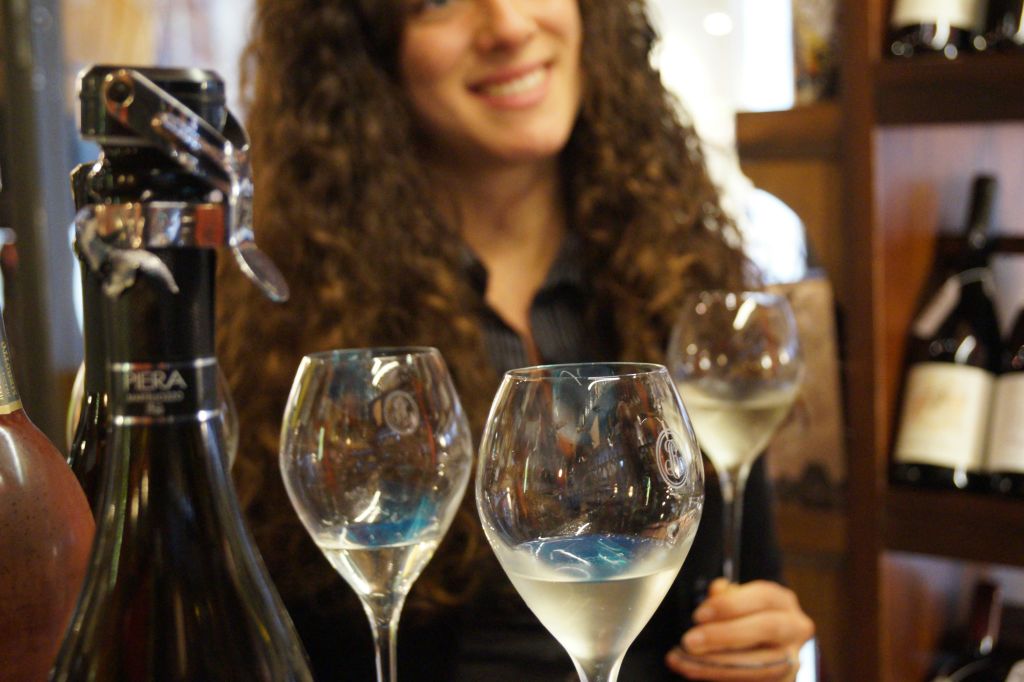 한 사람이 화이트 와인이 가득 담긴 병과 와인 잔 세 개를 배경으로 미소를 짓고 있습니다.