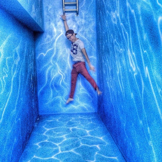 빨간색 바지와 흰색 셔츠를 입은 사람이 사다리에 물 같은 패턴의 파란색 벽에 매달려 있습니다.