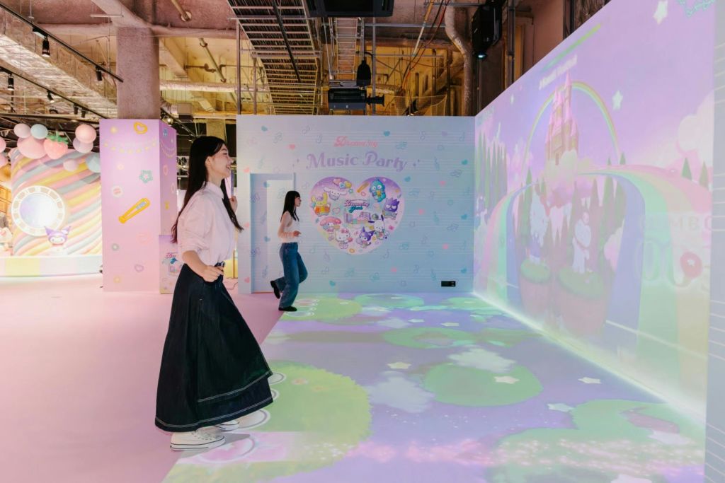 장식용 벽과 부드러운 조명이 있는 다채로운 파스텔 테마의 이벤트 공간 안을 걷고 있는 두 사람.