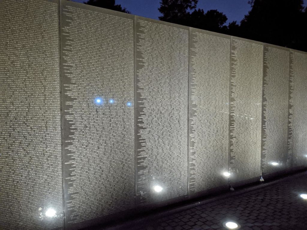 나무를 배경으로 어두운 하늘을 배경으로 여러 개의 기둥에 이름이 새겨진 조명 벽.