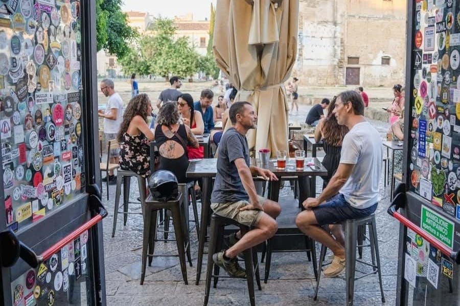 카페의 야외 테이블에 앉아 대화를 나누는 사람들. 테이블에 맥주잔이 놓여 있습니다. 도시 배경입니다.