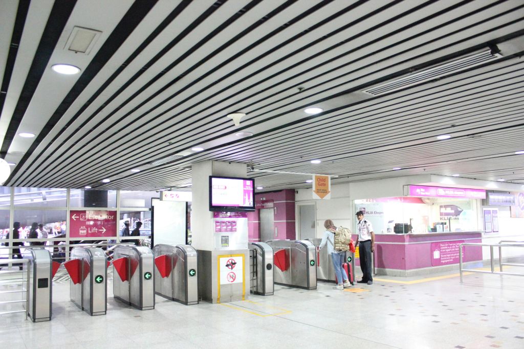 개찰구가 있는 지하철역 입구와 티켓 부스. 한 사람이 엘리베이터 표지판 옆에서 직원과 소통하고 있습니다.