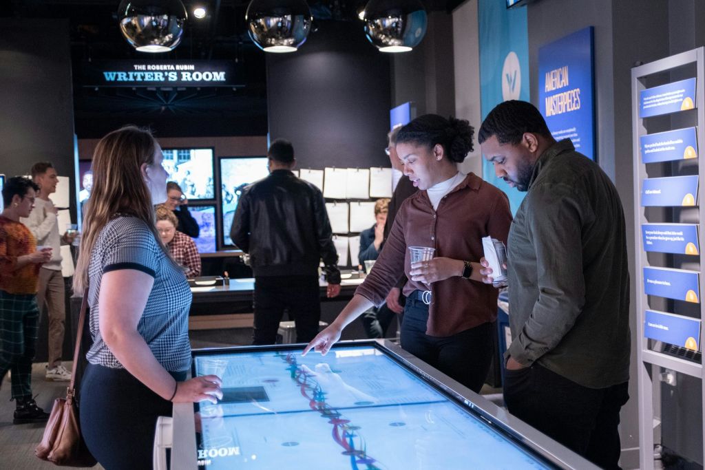 박물관에서 두 사람이 디지털 디스플레이 테이블을 배경으로 대화를 나눕니다.