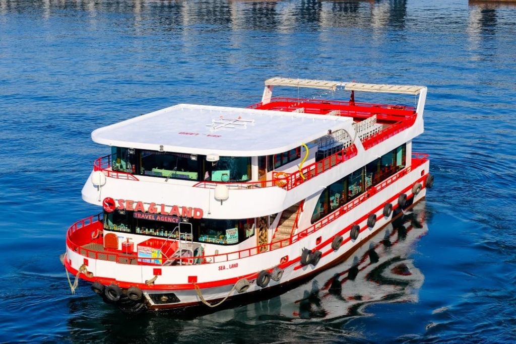 잔잔한 물가에 "Sea Land Travel Agency" 라는 이름의 빨간색과 흰색 페리 보트가 있으며, 데크와 창문이 보입니다.