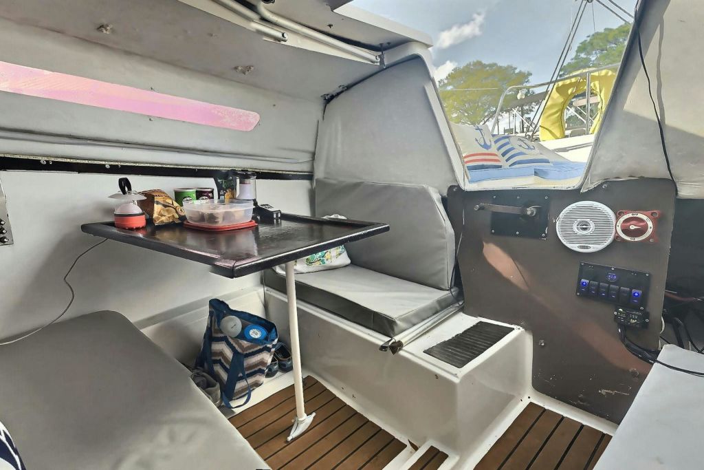 좌석이 있는 작은 보트의 내부, 접이식 테이블, 다양한 물품이 놓여 있습니다. 바닥에 가방이 있습니다.