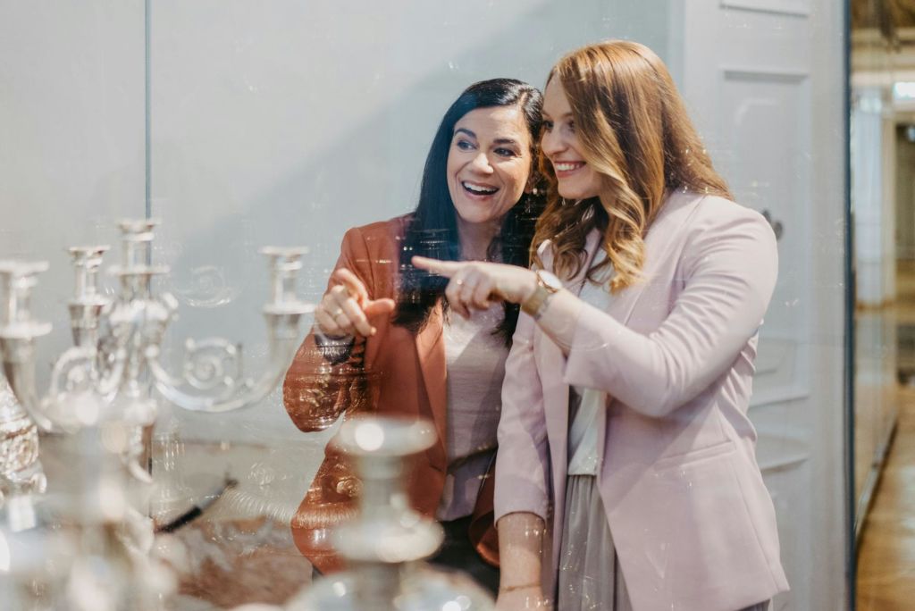 블레이저를 입은 두 여성이 눈앞에서 무언가를 가리키며 미소를 짓고 있습니다. 앞쪽에 흐릿한 물체가 있습니다.